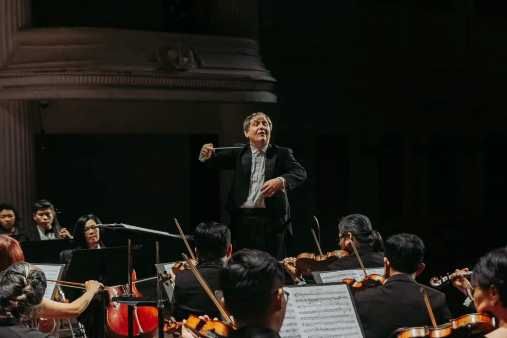Dyrygent Wojciech Czepiel podczas prowadzenia orkiestry symfonicznej na koncercie.